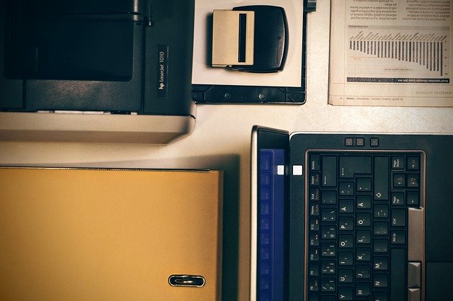 notebook na stole, pohled seshora, vedle tiskárna, razítko a nějaké tiskopisy
